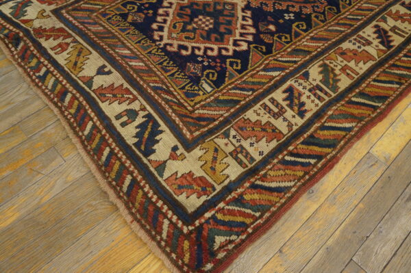 Navy blue geometric rug with wide cream and multi-colored borders on distressed wood planks.