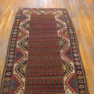 Long red runner rug with intricate geometric patterns and dark borders sits on light hardwood flooring.
