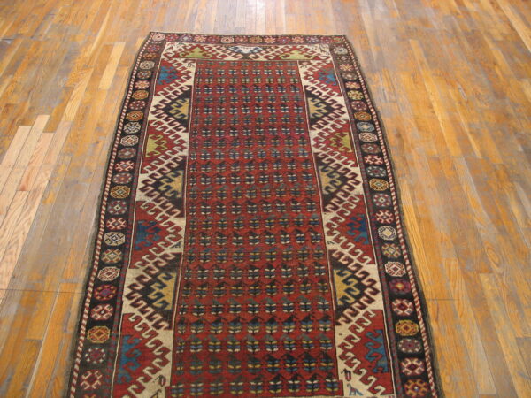 Long red runner rug with intricate geometric patterns and dark borders sits on light hardwood flooring.