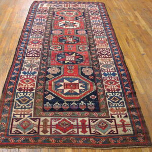 Geometric red, blue, and cream runner rug with central medallions resting on light wooden flooring.