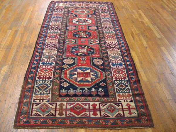 Geometric red, blue, and cream runner rug with central medallions resting on light wooden flooring.