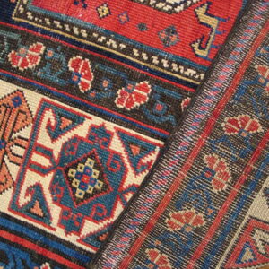 Section of a patterned rug in red, blue, black, and cream showing both pile and flatweave textures.