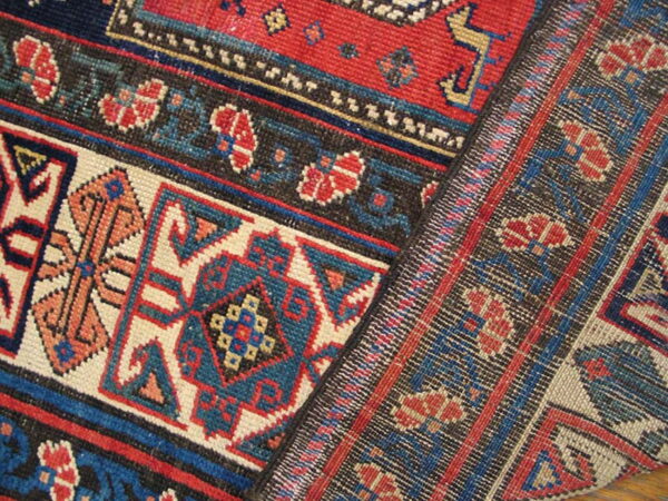 Section of a patterned rug in red, blue, black, and cream showing both pile and flatweave textures.