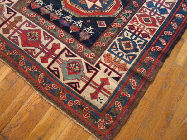 Geometric patterned rug in deep blue, red, cream, and olive tones shown on rustic wood flooring.
