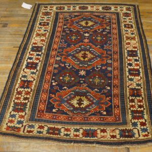 Traditional navy and rust rug with geometric motifs and borders rests on worn, light wood flooring.
