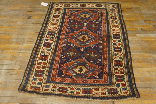Traditional navy and rust rug with geometric motifs and borders rests on worn, light wood flooring.