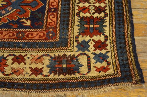 Close-up shows an intricate tribal rug corner in navy, red, and cream on distressed wood planks.