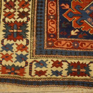 Close-up of a low-pile rug corner displaying geometric borders in navy, red, and cream on wood flooring.