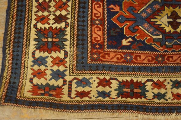 Close-up of a low-pile rug corner displaying geometric borders in navy, red, and cream on wood flooring.