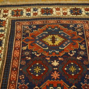 Detailed geometric rug in dark blue, rust red, and cream with a detailed main border on wood flooring.