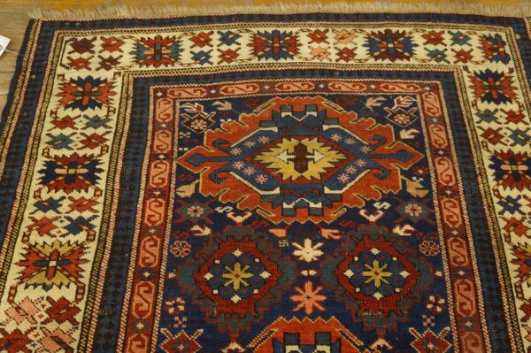 Detailed geometric rug in dark blue, rust red, and cream with a detailed main border on wood flooring.
