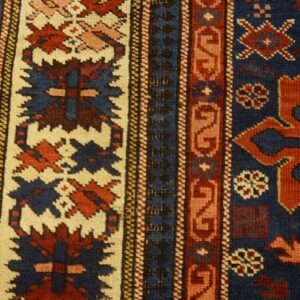 Geometric rug detail showing rust and indigo patterns within cream borders, resting on wood flooring.