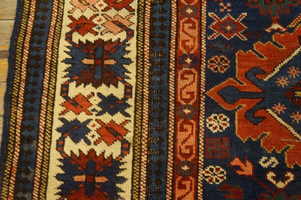 Geometric rug detail showing rust and indigo patterns within cream borders, resting on wood flooring.