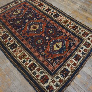 Navy and rust geometric rug with complex borders resting on distressed gray wood flooring.