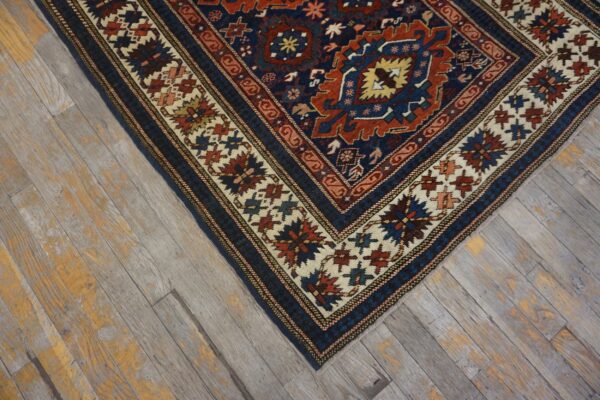 Navy blue, red, and cream geometric rug corner rests on weathered gray and orange wood planks.