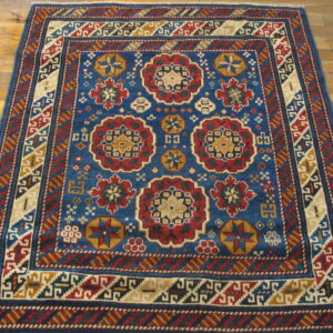 Blue rug with red and gold geometric medallions and patterned borders resting on light wood flooring.