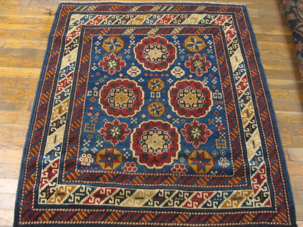 Blue rug with red and gold geometric medallions and patterned borders resting on light wood flooring.