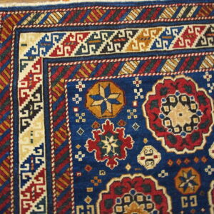 Blue, red, and gold patterned rug corner showing geometric borders and medallions on a wood floor.