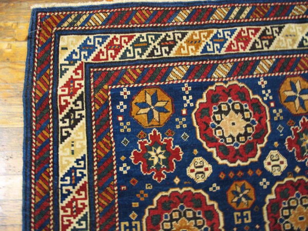 Blue, red, and gold patterned rug corner showing geometric borders and medallions on a wood floor.