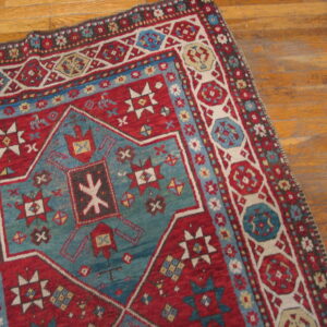 Geometric red rug with a large blue-green central motif lying on light brown wood planks.