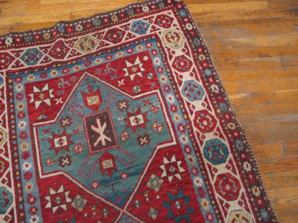 Geometric red rug with a large blue-green central motif lying on light brown wood planks.