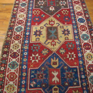 Red, blue, and tan geometric runner rug with complex medallions displayed on a wood floor.