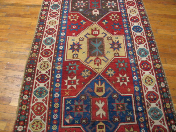 Red, blue, and tan geometric runner rug with complex medallions displayed on a wood floor.