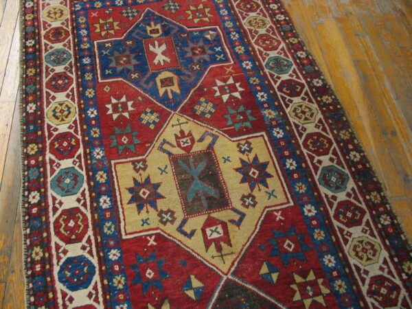 Red and blue tribal rug with geometric medallions and intricate borders rests on worn hardwood flooring.