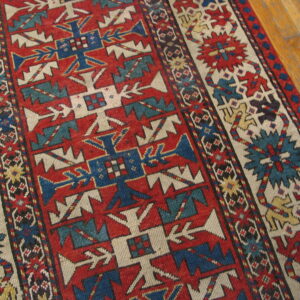 Low-pile rug with geometric patterns in red, blue, and ivory rests on a polished wood floor.