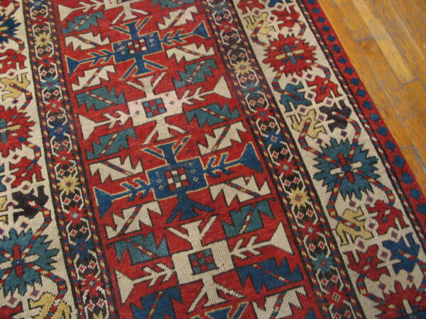 Low-pile rug with geometric patterns in red, blue, and ivory rests on a polished wood floor.