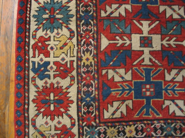 Geometric patterned rug detail showing red, blue, cream, and yellow motifs next to wood flooring.