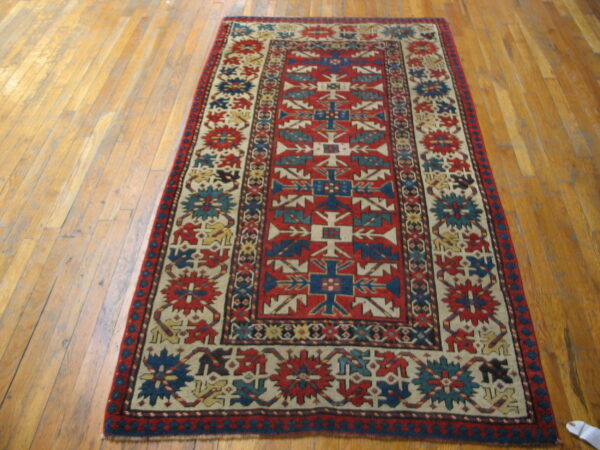 Red field rug with navy blue and cream geometric patterns lays on light brown wood planks.