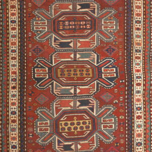 Vertical rug with a rust red field, featuring complex navy blue, gold, and cream geometric motifs.