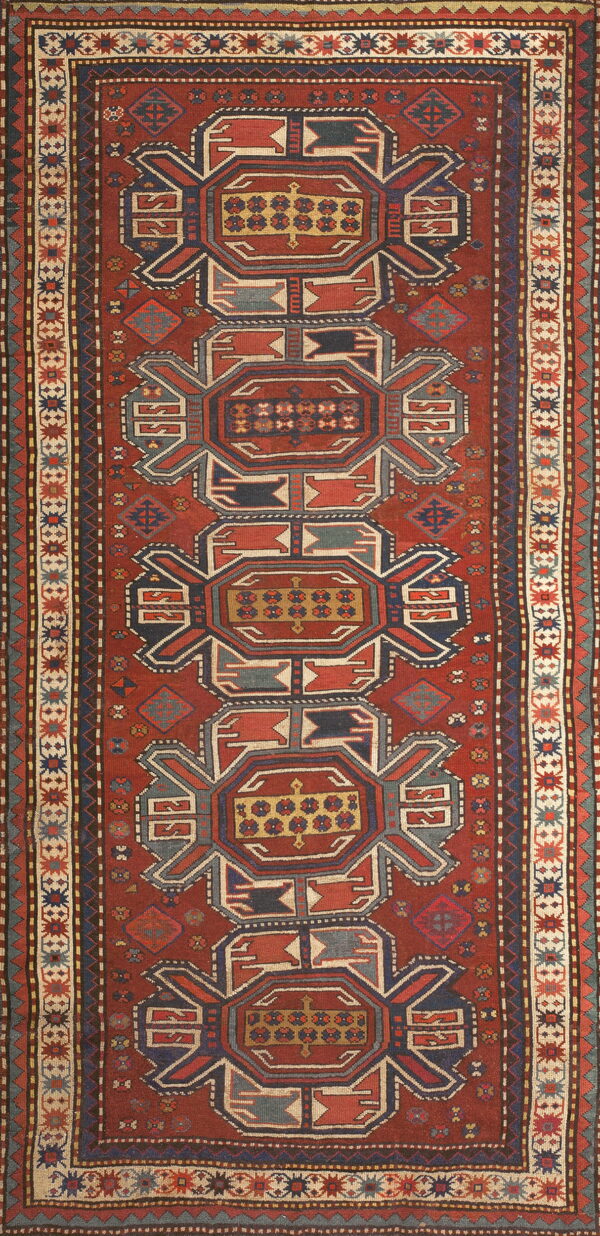 Vertical rug with a rust red field, featuring complex navy blue, gold, and cream geometric motifs.