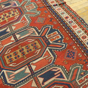 Red rug displaying bold geometric medallions and borders in navy, teal, and gold on a light wood floor.