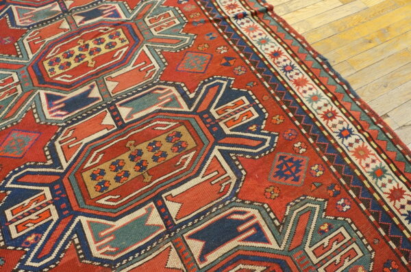 Red rug displaying bold geometric medallions and borders in navy, teal, and gold on a light wood floor.