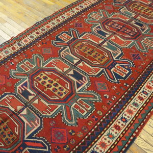A low-pile red runner featuring repeating geometric medallions and multiple borders on light hardwood floors.