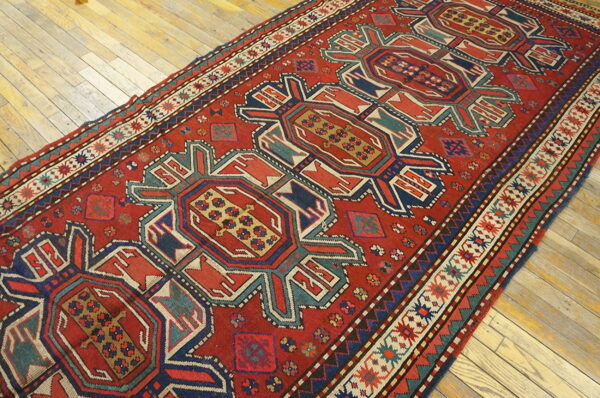 A low-pile red runner featuring repeating geometric medallions and multiple borders on light hardwood floors.