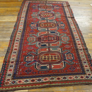 A red runner rug with navy blue and teal geometric tribal motifs lies on worn wood floors.