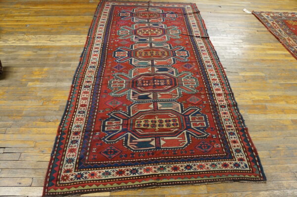 A red runner rug with navy blue and teal geometric tribal motifs lies on worn wood floors.