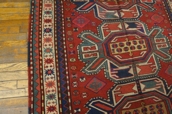 A red rug with complex blue, teal, and cream geometric designs lies on light wood planks.