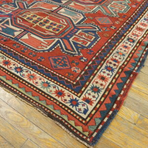 Low-pile red rug with complex blue and cream geometric designs lies on light distressed hardwood planks.