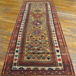 Low-pile geometric runner in gold, rust, and blue on a worn light brown plank wood floor.