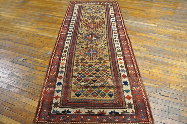 Low-pile geometric runner in gold, rust, and blue on a worn light brown plank wood floor.