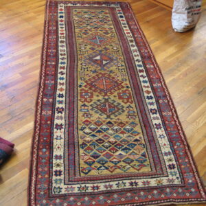 Geometric runner rug in red, gold, and blue lying on a distressed plank hardwood floor.