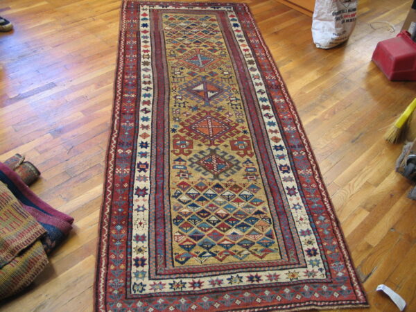 Geometric runner rug in red, gold, and blue lying on a distressed plank hardwood floor.