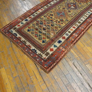 Gold and red geometric runner rug rests diagonally on distressed yellow plank hardwood flooring.