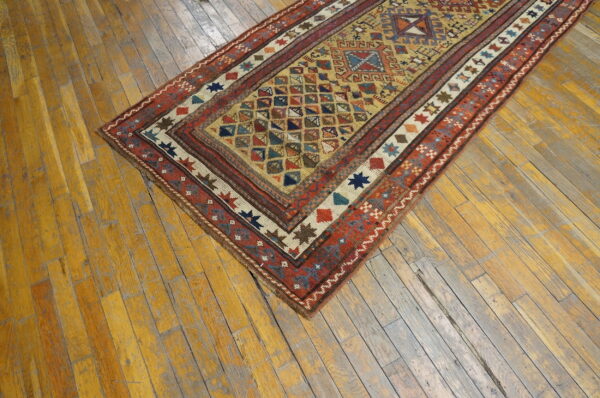 Gold and red geometric runner rug rests diagonally on distressed yellow plank hardwood flooring.