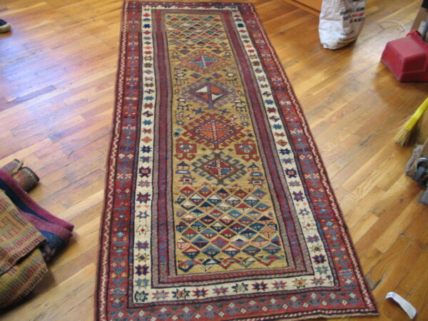 Overhead view of a geometric runner rug with red borders and a gold field on plank wood flooring.