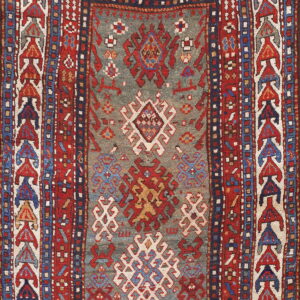 Geometric rug with a slate gray-blue center containing tribal motifs and complex multi-layered red borders.